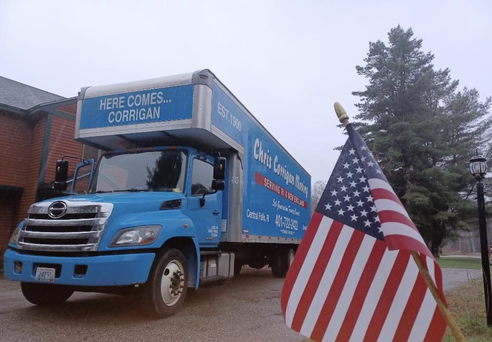 A blue truck with an american flag parked in front of a house, representing a moving company.